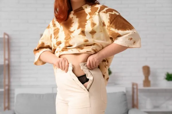 Image of woman trying to do her trousers up after pregnancy weight gain Cambridge